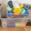 Clear plastic container filled with colorful silicone cups on a wooden floor.