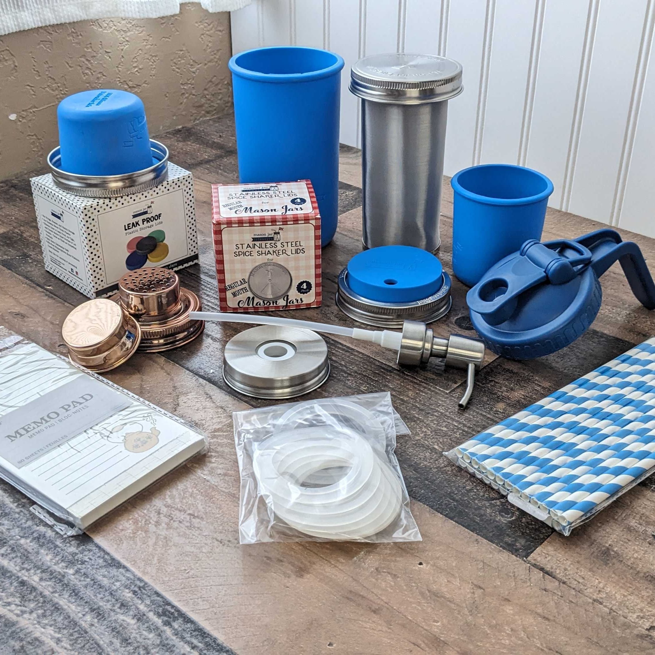 Collection of stainless steel and blue travel mugs and accessories on a wooden surface.