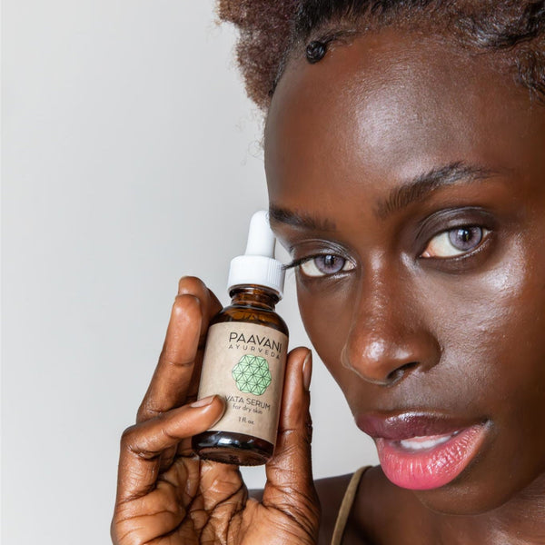 Woman holding a bottle of Paavani Ayurveda serum close to her face against a plain background