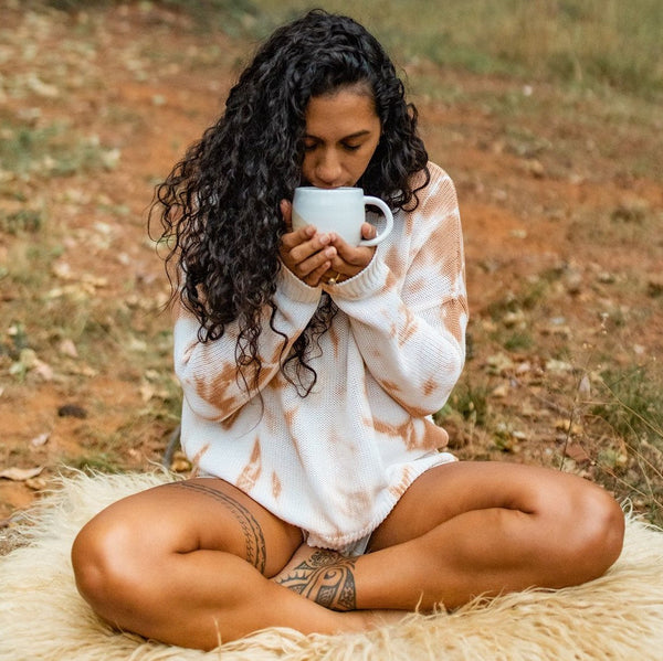 Woman sitting outdoors holding a mug, wrapped in a tie-dye blanket