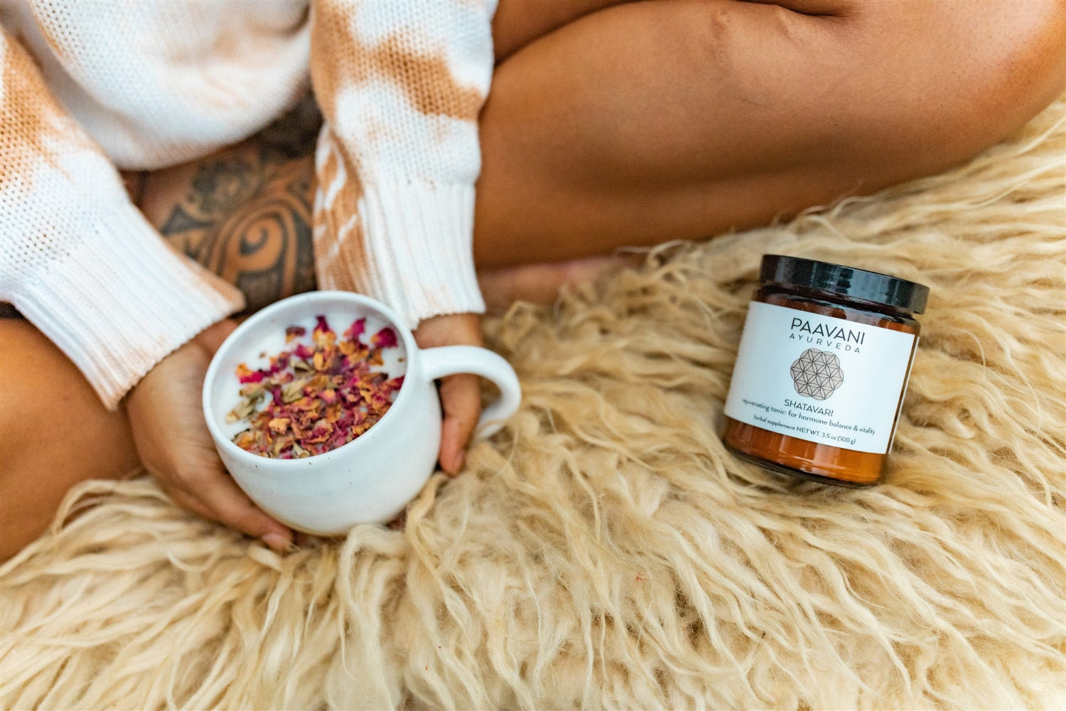 Person holding a mug with dried flowers, sitting on a fluffy surface next to a Puuvana jar.