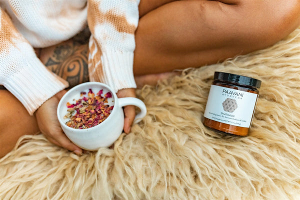 Person holding a mug with dried flowers, sitting on a fluffy surface next to a Puuvana jar.