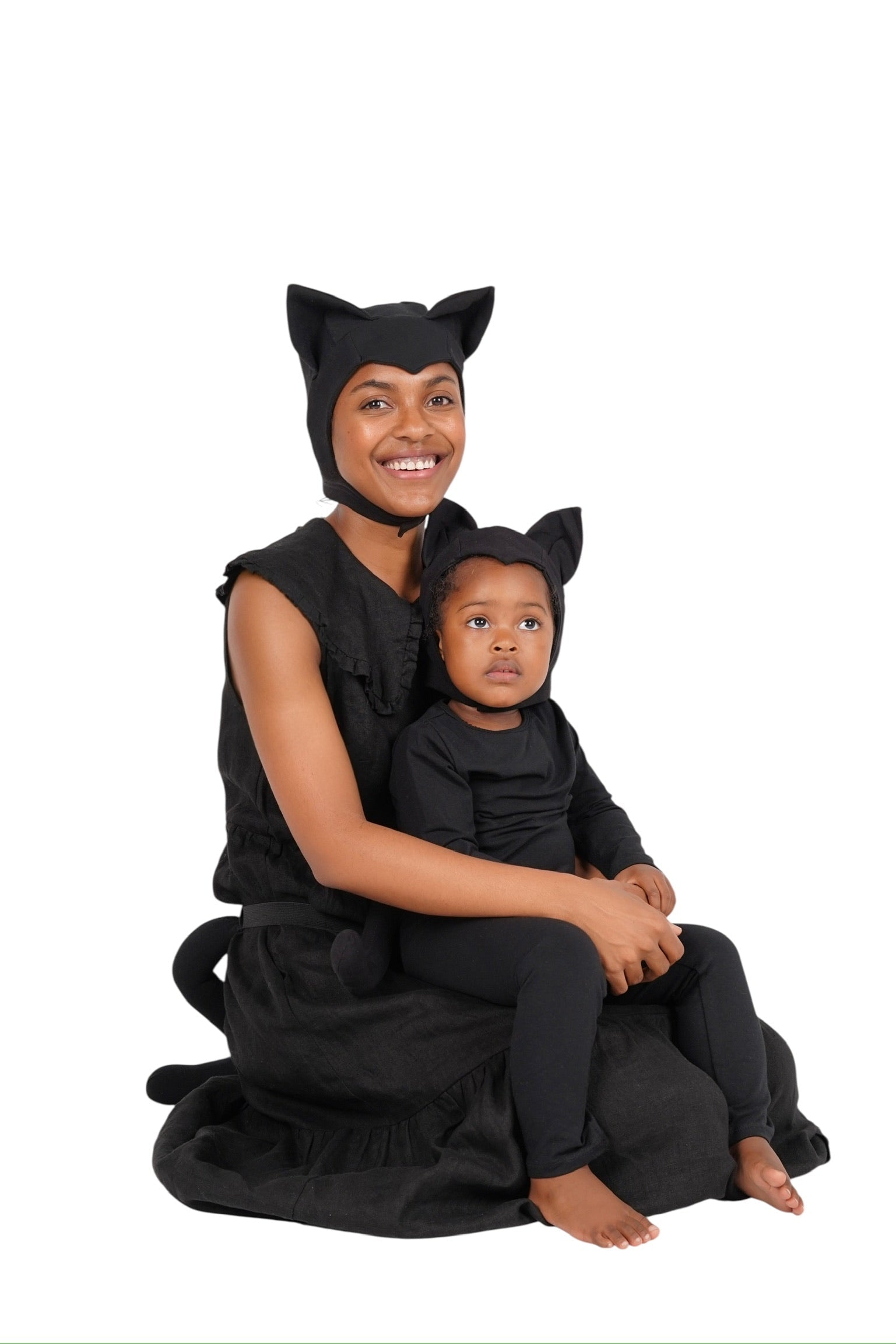Woman and child in black cat costumes sitting together on a white background