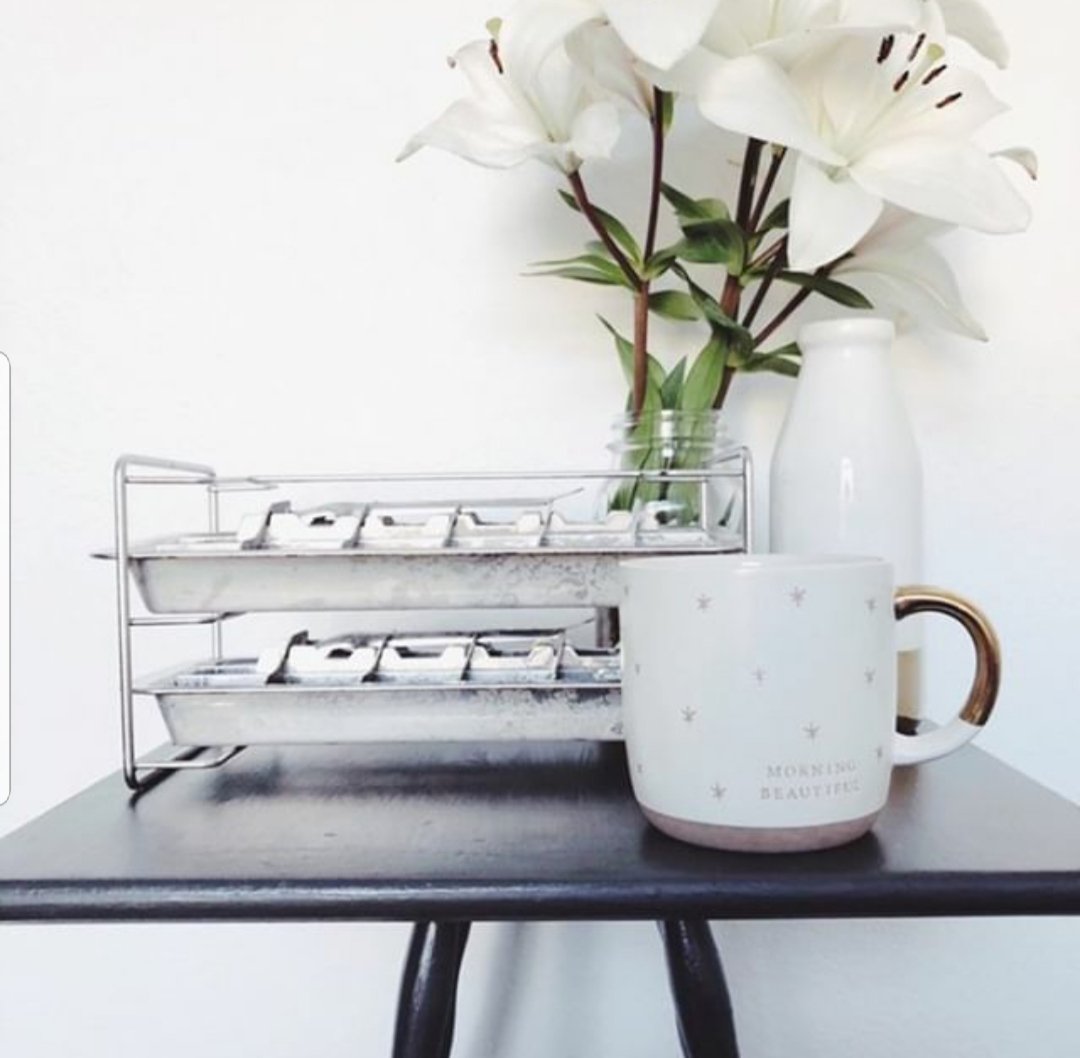 White mug with brown handle on a black surface, next to a white vase and glass container with greenery.