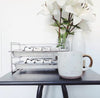 White mug with brown handle on a black surface, next to a white vase and glass container with greenery.