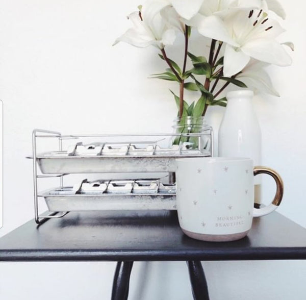White mug with brown handle on a black surface, next to a white vase and glass container with greenery.