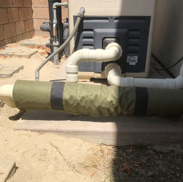 Outdoor HVAC system with pipes and a green insulation wrap on a concrete floor.