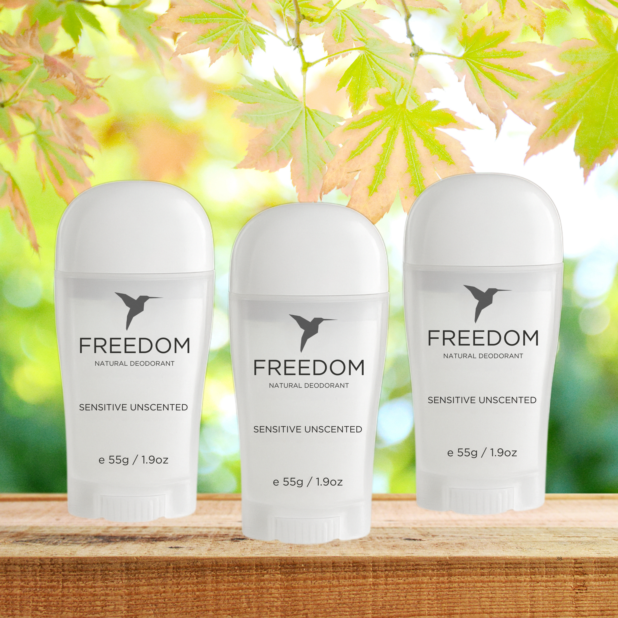 Three bottles of Freedom natural deodorant on a wooden surface with a blurred green leafy background