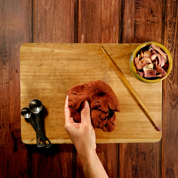 Hand holding a piece of meat on a wooden cutting board with a small bowl of additional meat and measuring spoons.