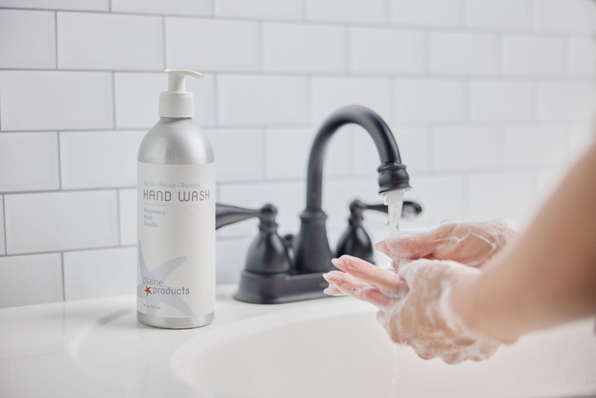 Person washing hands with soap in a sink next to a bottle of hand wash.