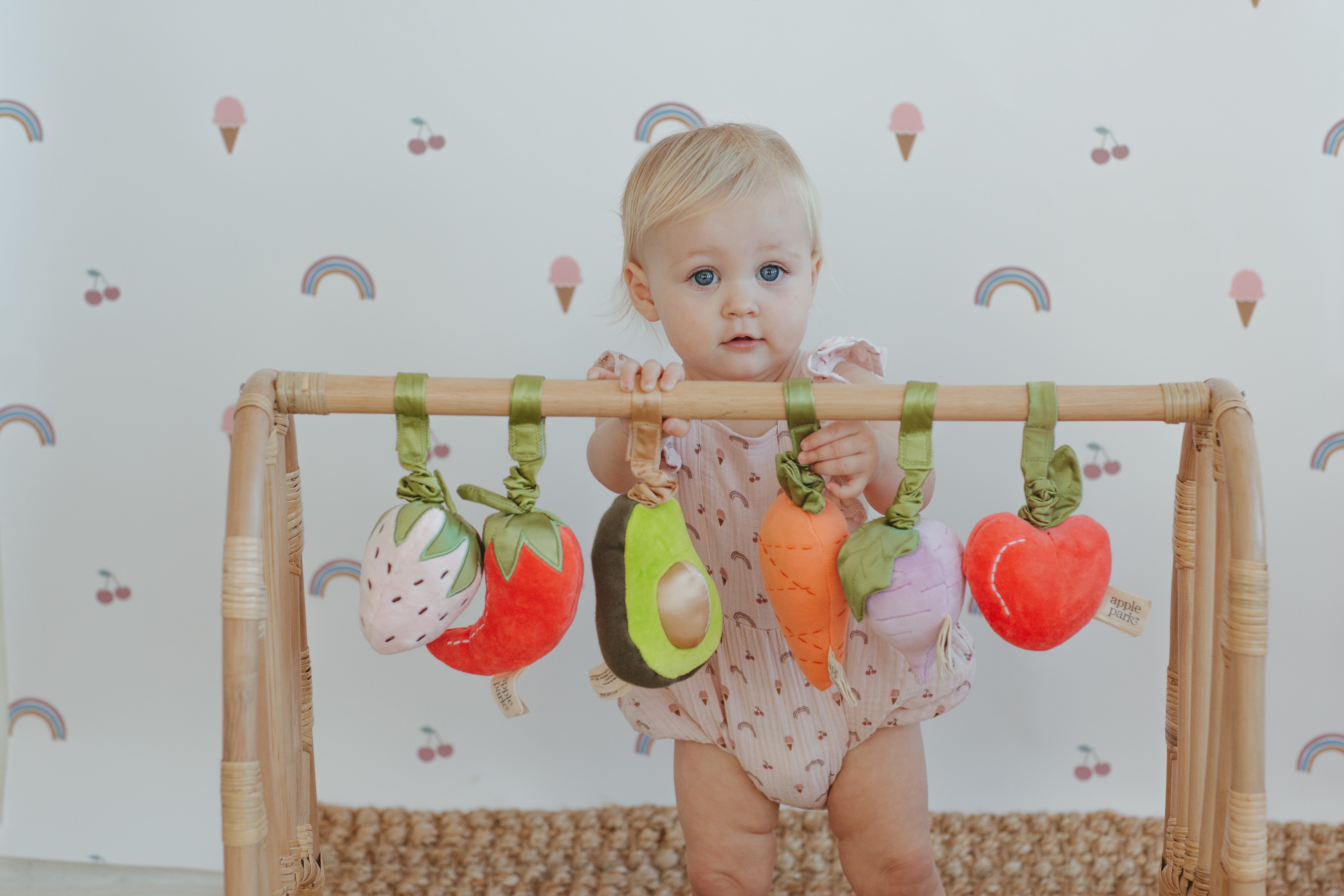 Apple Park organic muslin baby romper in rainbows and ice cream print styled with fruit and veggie stroller toys