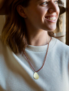 Close-up of hammered oval brass pendant with red glass beads on white background