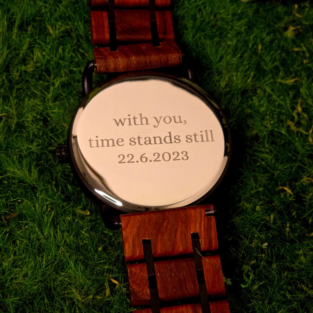 A wooden watch with a black dial and brown strap, displayed on a natural wood surface.