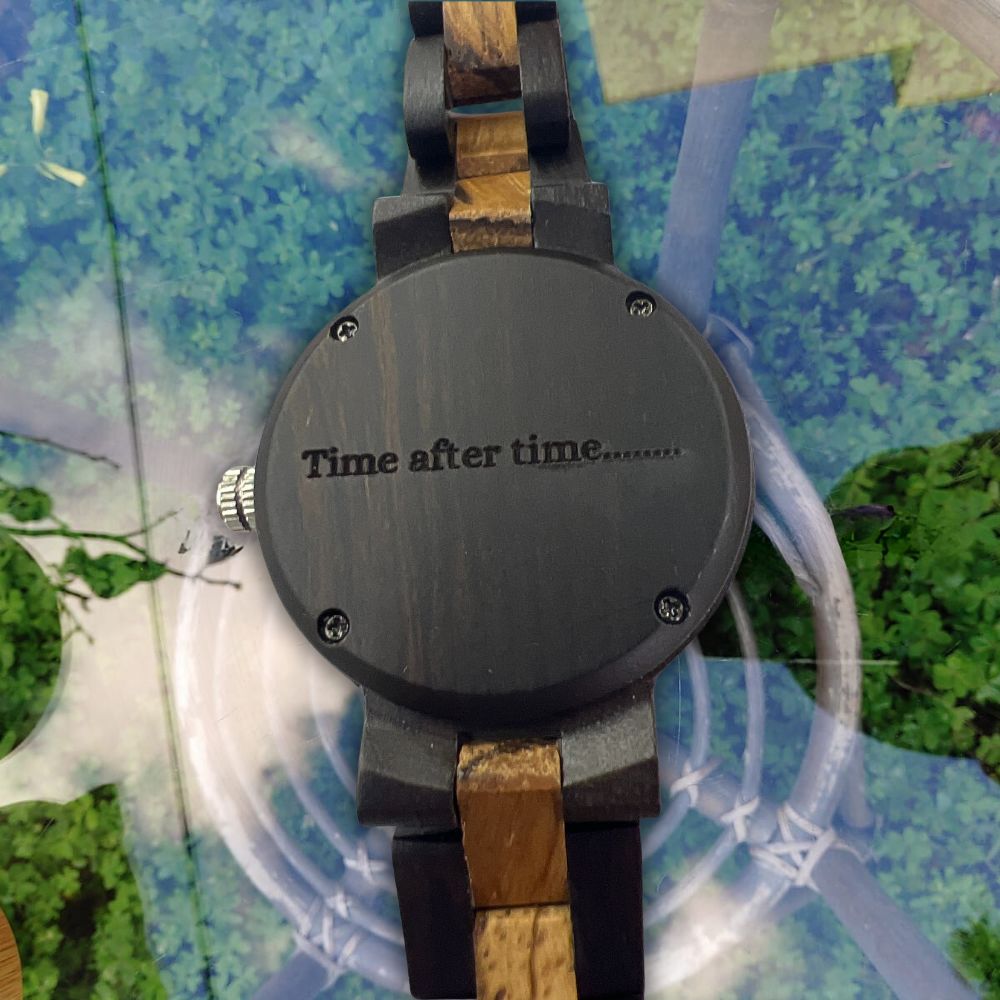 A wooden watch with a dark gray round case engraved with 'Time after time.