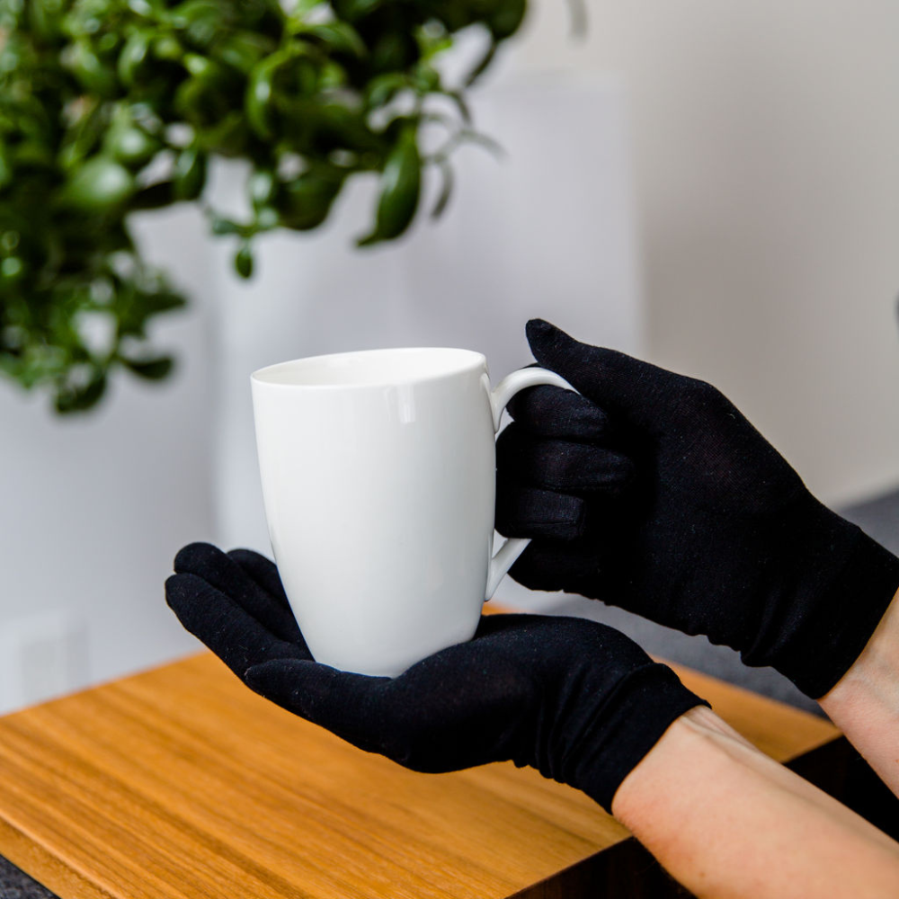 Adult wearing black Remedywear eczema gloves while holding a mug, showing comfortable everyday fit for psoriasis and eczema on hands