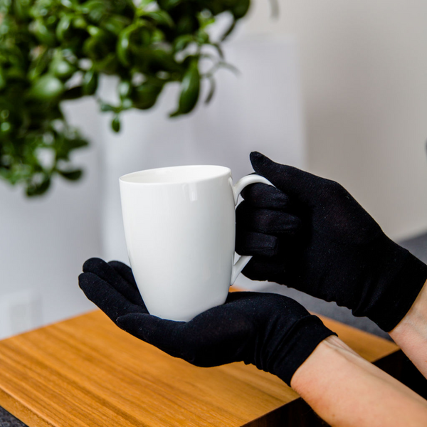 Adult wearing black Remedywear eczema gloves while holding a mug, showing comfortable everyday fit for psoriasis and eczema on hands