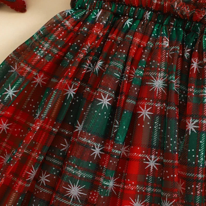 A close-up of a pleated fabric skirt featuring a festive Christmas plaid pattern in red and green with white snowflake motifs.