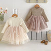 Two children's dresses hanging on a white surface with a neutral background.