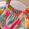 A close-up of a colorful floral-patterned top with a gathered elastic neckline, featuring pink, yellow, green, and blue tones.