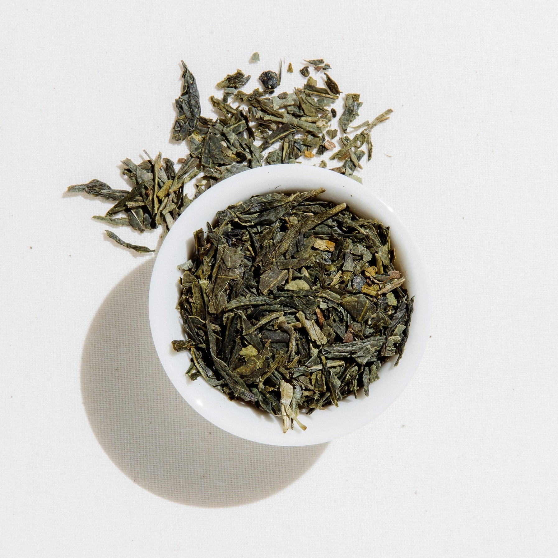 Loose leaf organic sencha green tea from Art of Tea in a white bowl, showing deep green dried tea leaves