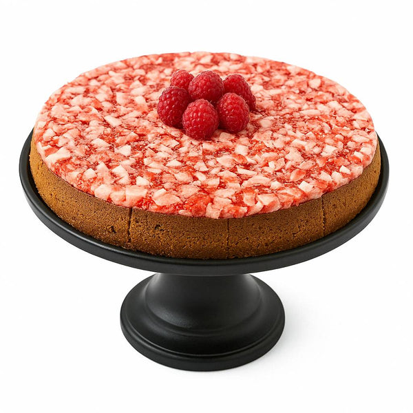 Round cake with a red and white textured top and raspberries on a black cake stand against a white background