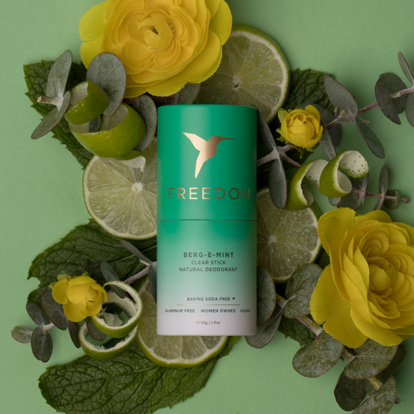 Freedom deodorant stick surrounded by yellow flowers and lime slices on a green background