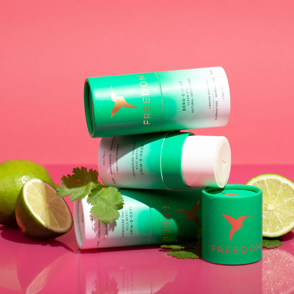 Green and white cylindrical products with 'Freedom' branding on a pink background with limes.
