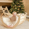 Child sitting in a wooden rocking chair with a decorated Christmas tree in the background.