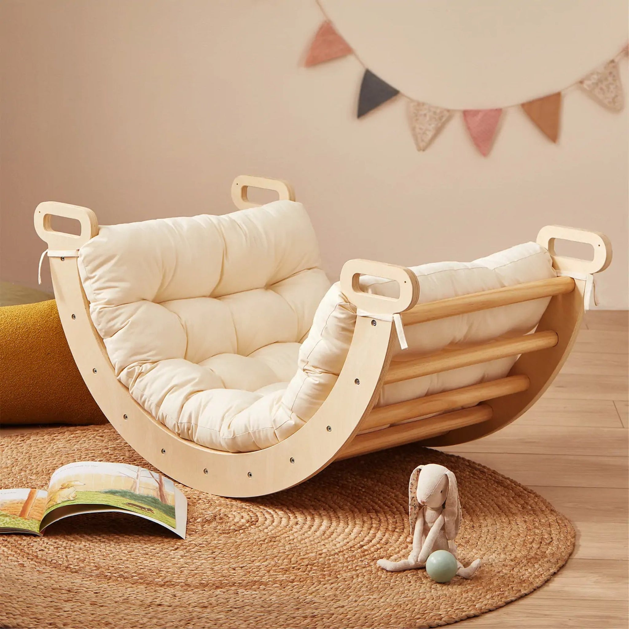 Wooden baby rocker with a white cushion on a wooden floor, surrounded by toys and books.