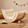 Wooden baby rocker with a white cushion on a wooden floor, surrounded by toys and books.
