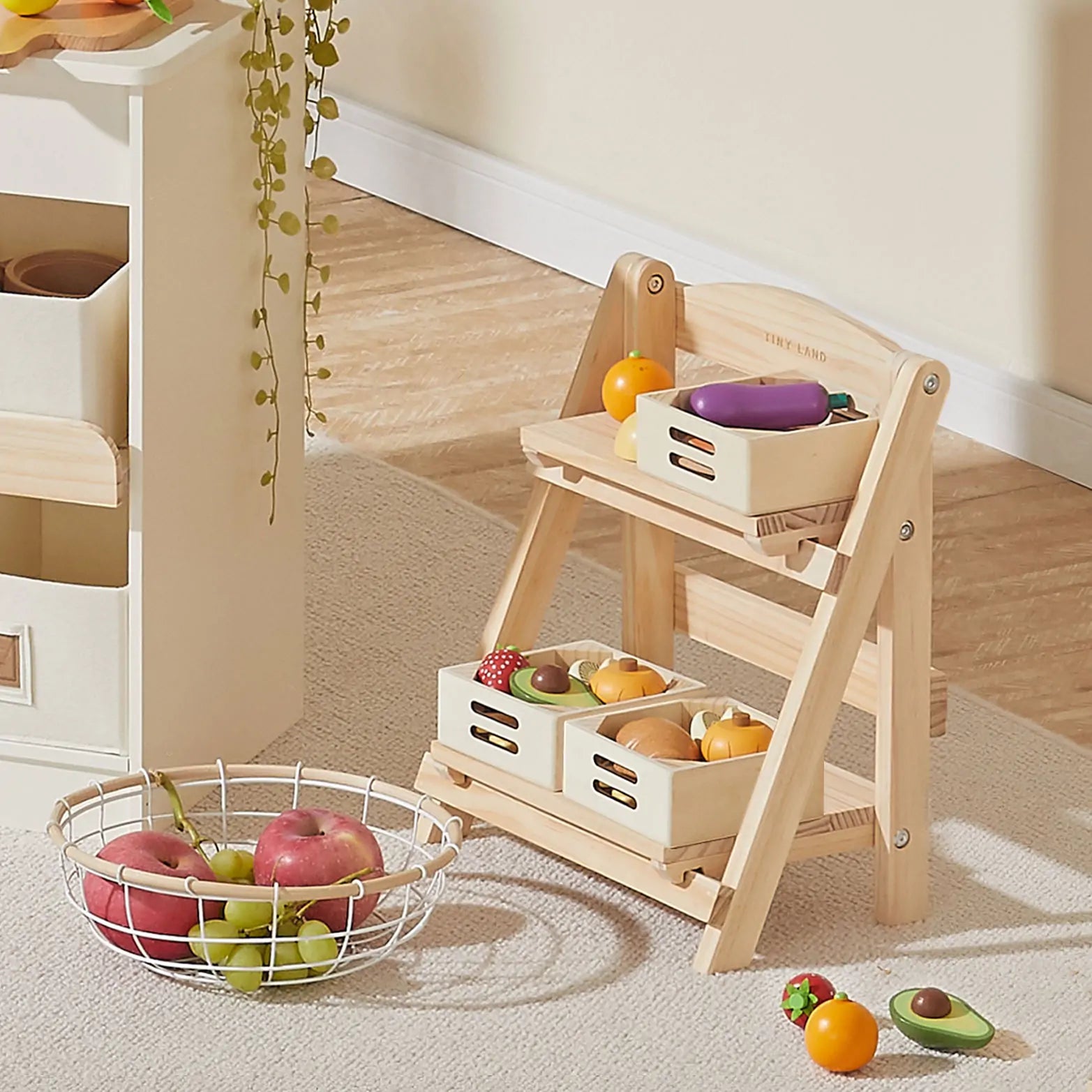 Wooden toy kitchen set with fruits and vegetables on a carpeted floor.