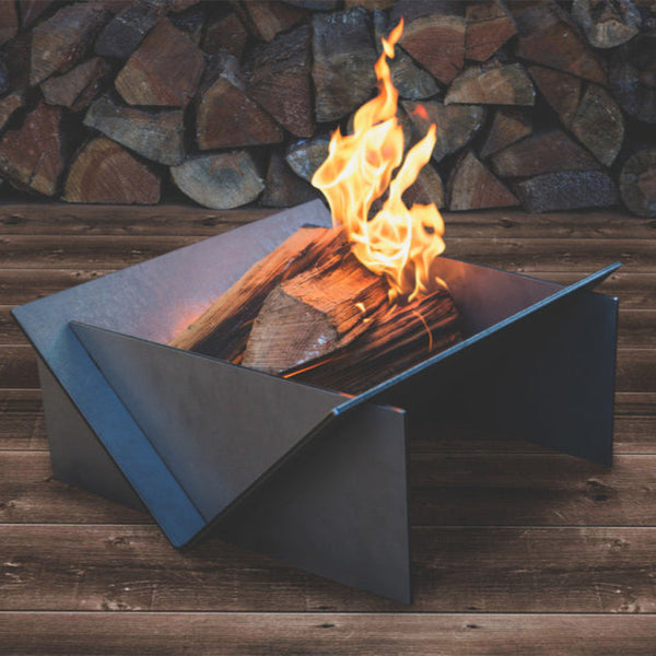 Metal fire pit with flames against a stone wall