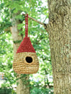Woven birdhouse with a red roof hanging from a tree branch.