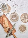 Jute coasters on a light surface with a wooden cutting board and bread.