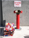 Red standpipe with a colorful quilt draped over it against a gray wall with a 'STAND PIPE' sign.