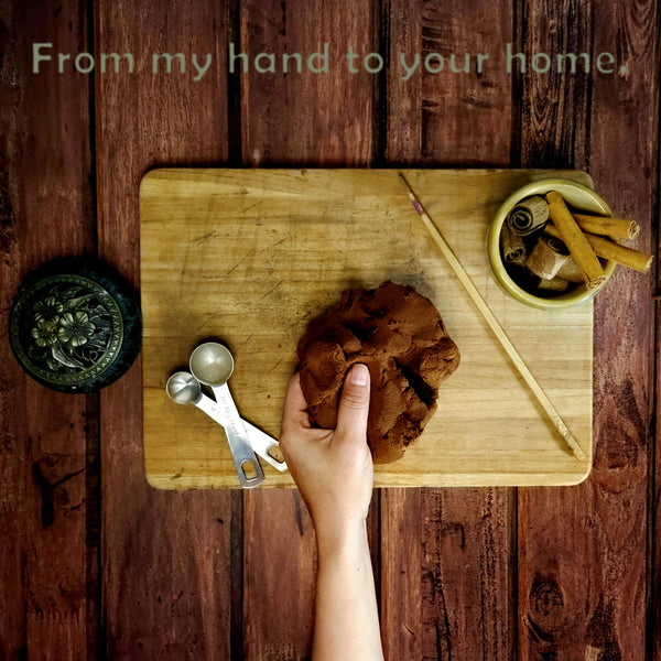 Hand holding a ball of dough on a wooden cutting board with measuring cups and a bowl of ingredients.