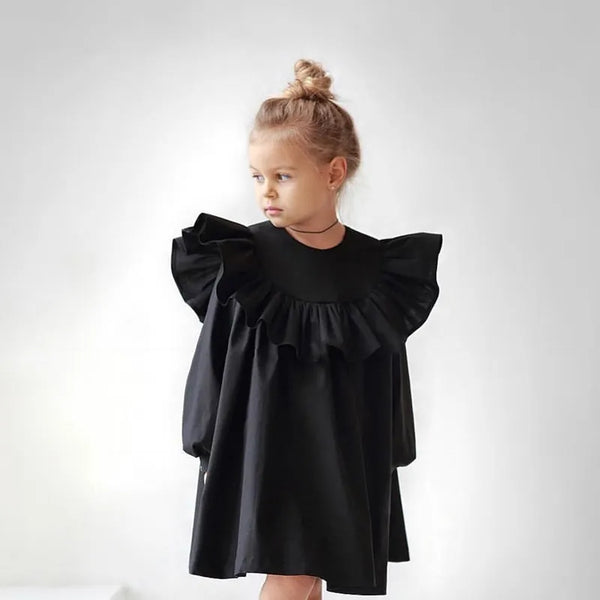 Young girl wearing a black dress with ruffled sleeves on a white background
