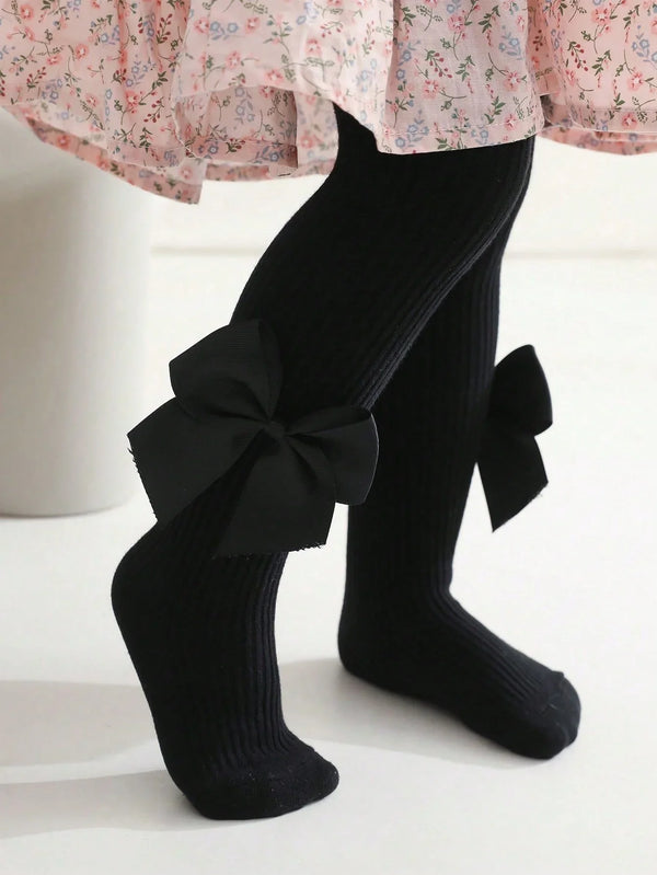 Black knee-high socks with a large bow worn by a person, on a white background