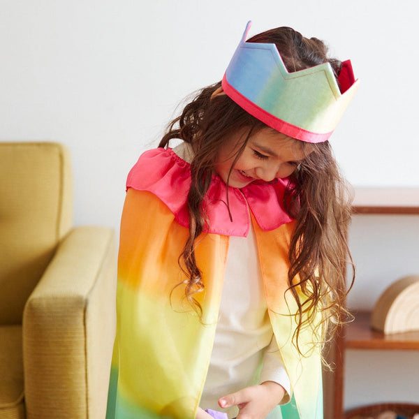 Child wearing a colorful costume with a rainbow headband in a room.