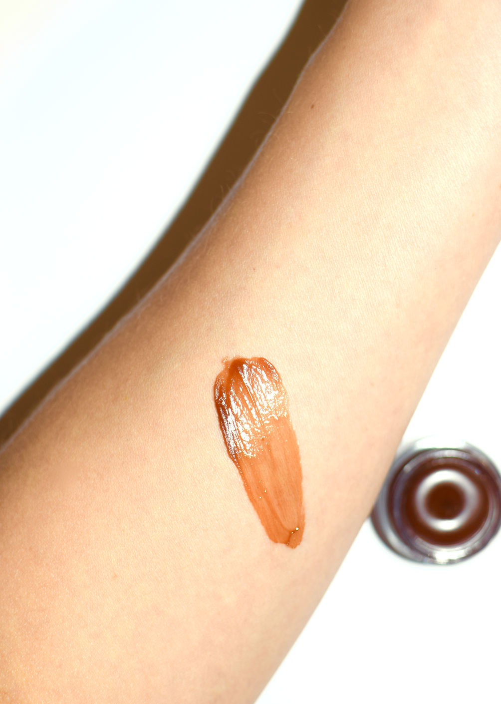 Lip balm swatch on a person's arm with a close-up of the lip balm container.