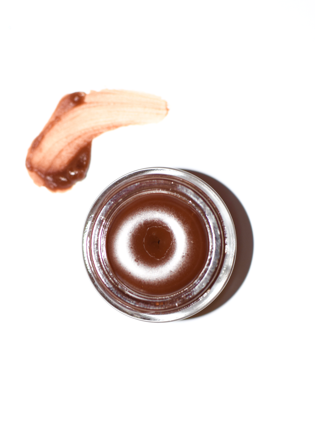 Small jar of brown cream with a swatch on a white background
