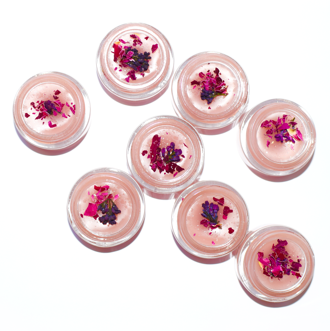 Set of small containers with pink lip balm and flower petals on a white background
