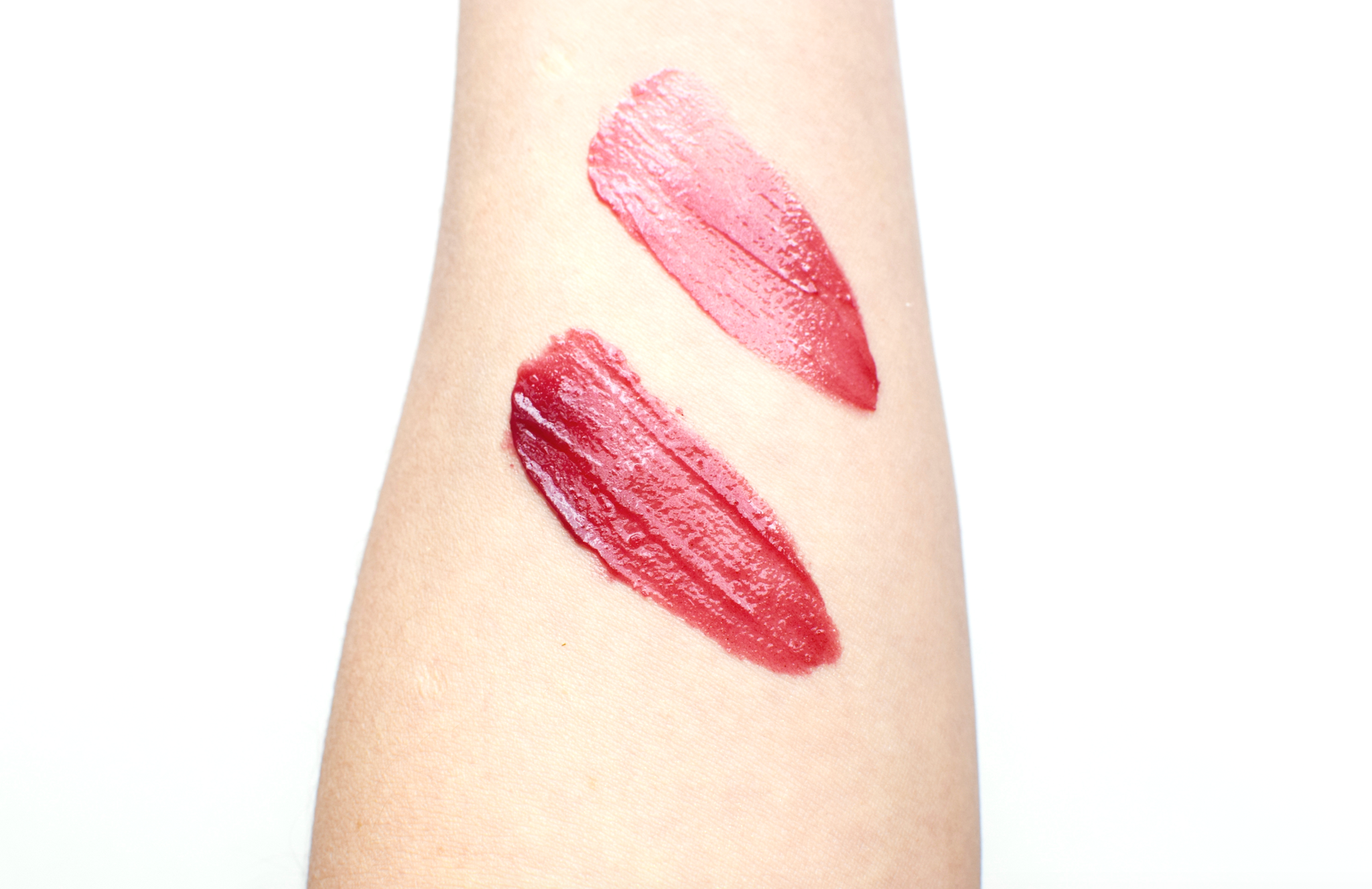 Two pink lipstick swatches on a person's arm against a white background