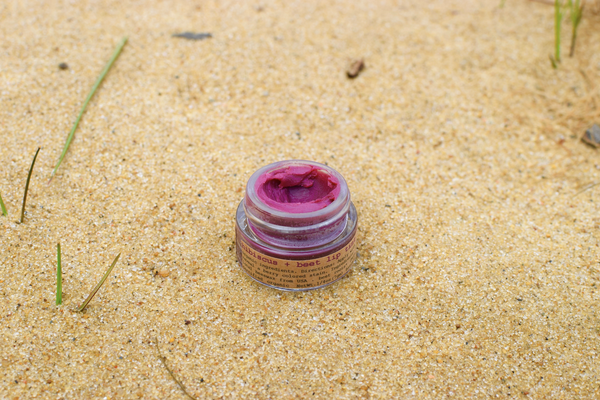 Makeup product with pink lid and label on sandy surface