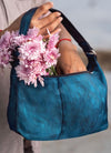 Blue handbag with pink flowers held by a person against a neutral background