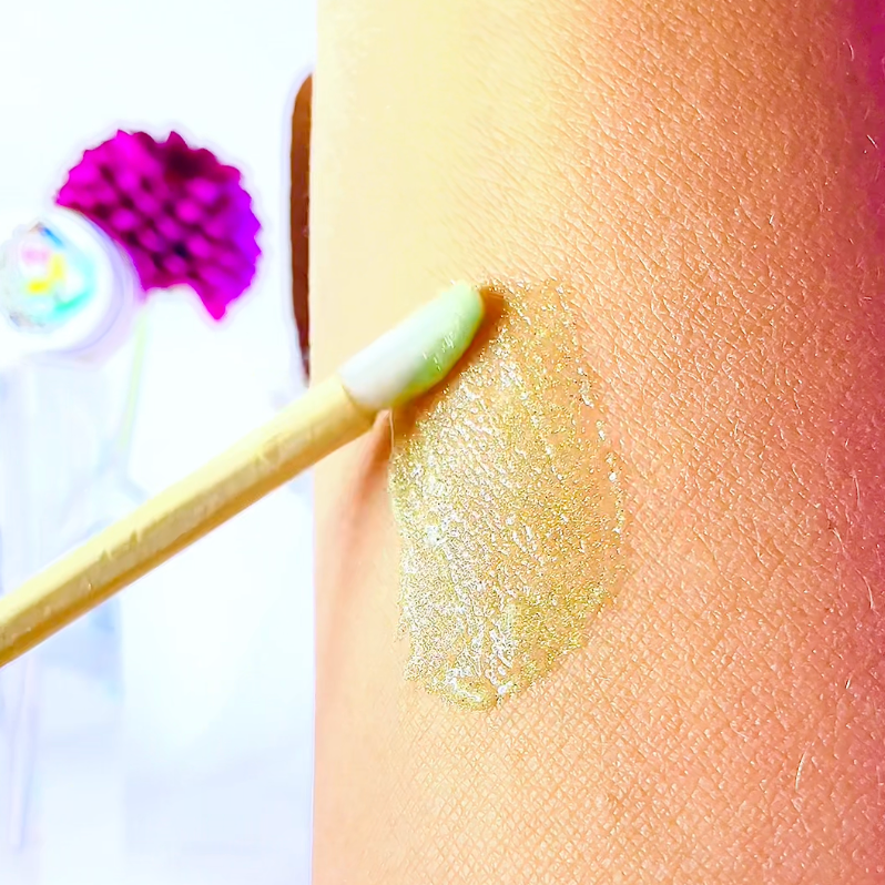 Close-up of a hand applying a green cream to a person's arm with a blurred background.