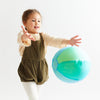 Child in a green dress holding a large inflatable ball with a white background