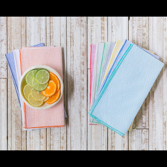 Set of colorful kitchen towels with a bowl of sliced fruit on a wooden surface
