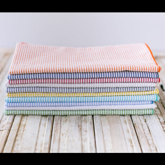Close-up of seersucker cloth napkins in assorted colors stacked together, highlighting the cotton blend fabric and puckered texture