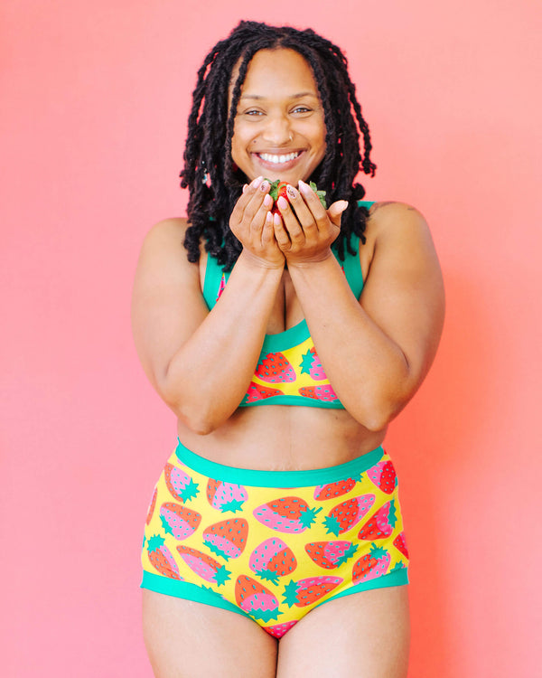 Woman wearing a colorful swimsuit with fruit patterns against a pink background